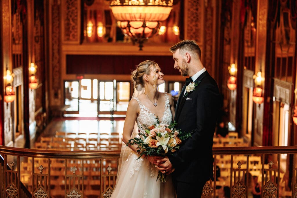 Bride and groom pose for a photo on a balcony over looking their ceremony space at the Warner theater